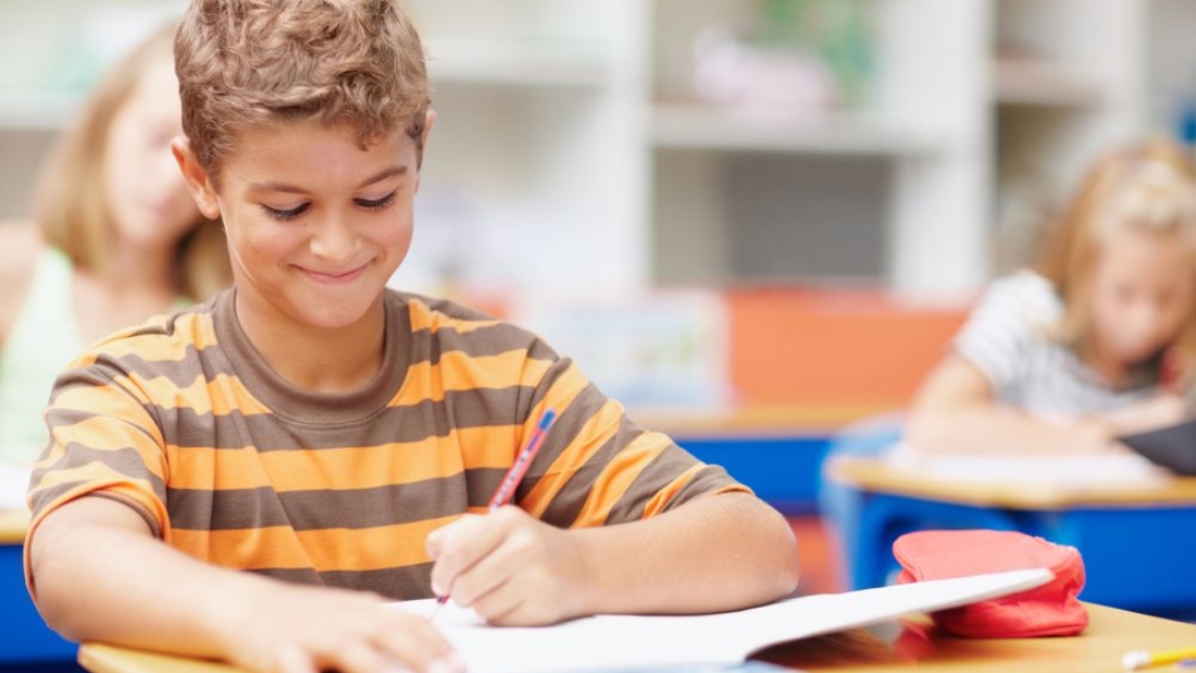 Writing, school and child in classroom for learning, education and lesson for development. Happy student, academy and young boy with stationery for test, creativity and assignment for knowledge.