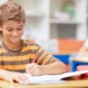 Writing, school and child in classroom for learning, education and lesson for development. Happy student, academy and young boy with stationery for test, creativity and assignment for knowledge.